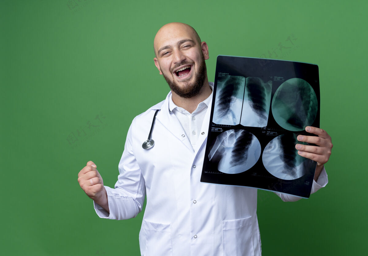 长袍快乐的年轻男医生穿着医用长袍和听诊器拿着x光片 在绿色背景上显示“是”的手势穿手势男性