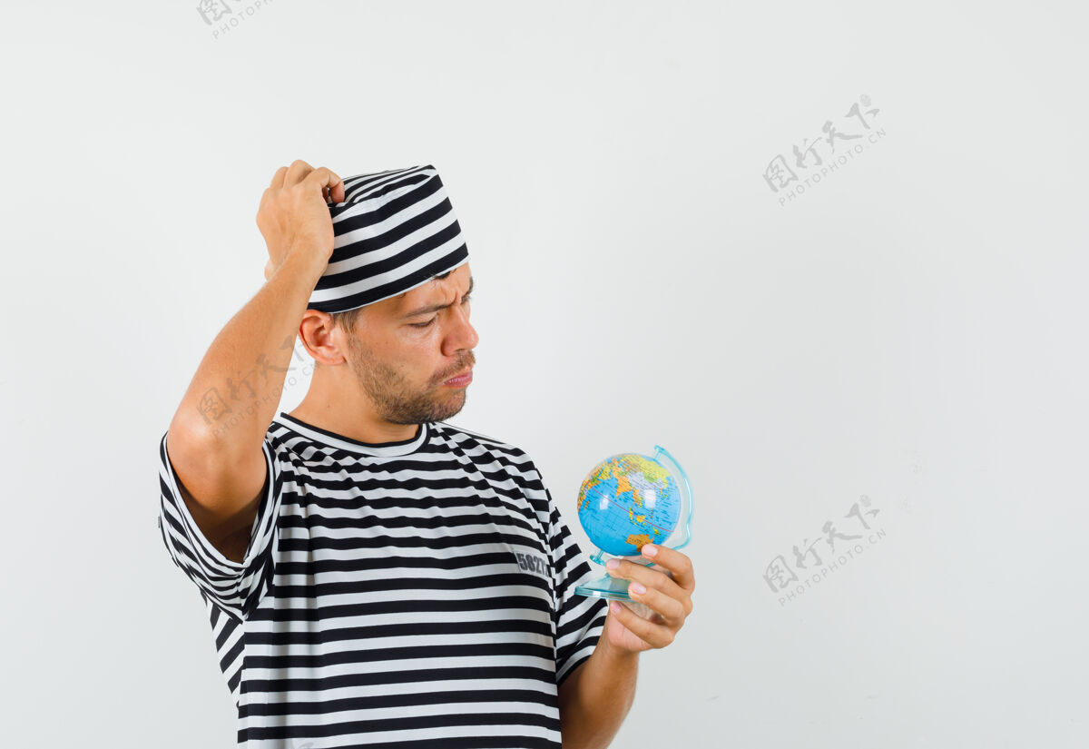 条纹年轻人拿着地球仪 戴着条纹t恤帽思考 看上去很小心思考休闲帽子