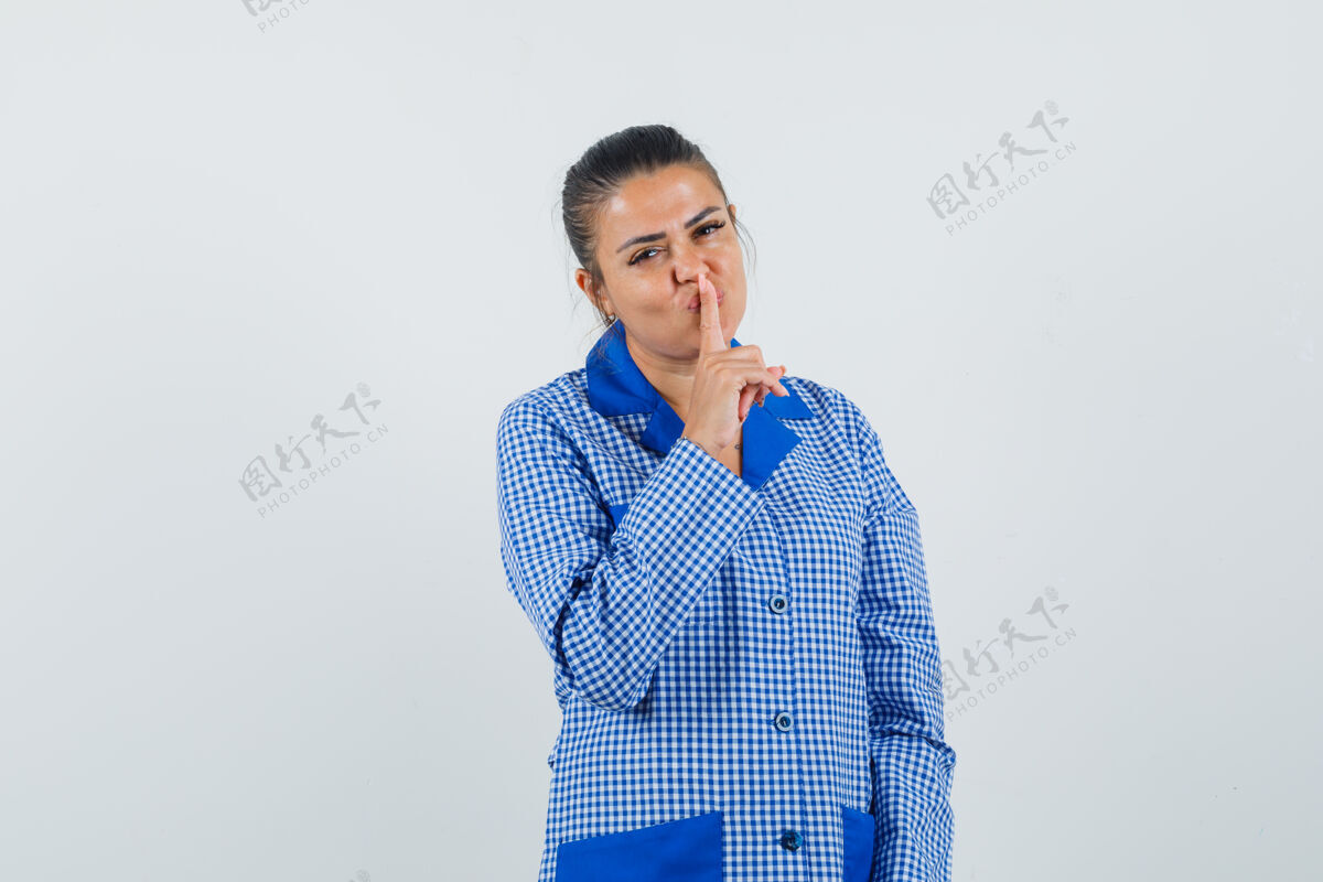 方格布身穿蓝色方格睡衣衬衫的年轻女子将食指放在嘴唇上 表现出沉默的姿态 看起来很漂亮 前视图模特自然皮肤