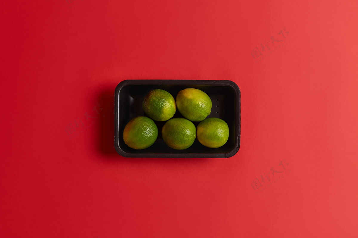 小新鲜青柠可在超市或市场上出售 黑色包装 红色背景下隔离成熟水果可用于制作果酱 柠檬水 鸡尾酒 夏季酸饮料自然光香橼水果素食