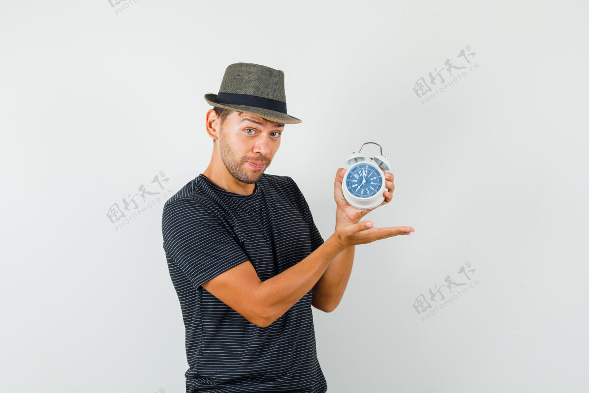 办公室年轻的男人戴着t恤帽子展示闹钟 看起来很快乐T恤时钟商务摄像头