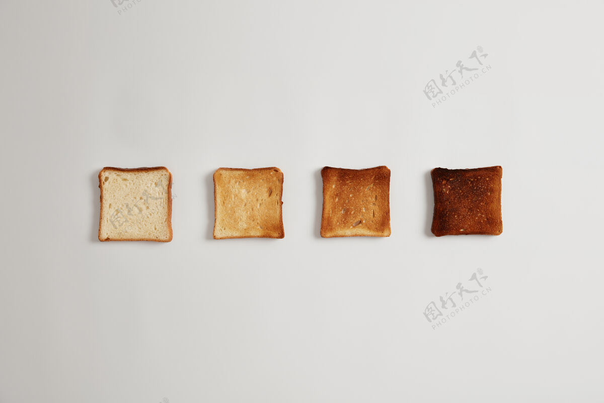 烤四片面包片 从未吃到烧焦 放在烤面包机里 靠着白色的表面排成一排一套烤面包片 用来做美味的硬皮三明治美味的早餐 烹饪食物新鲜卡路里块