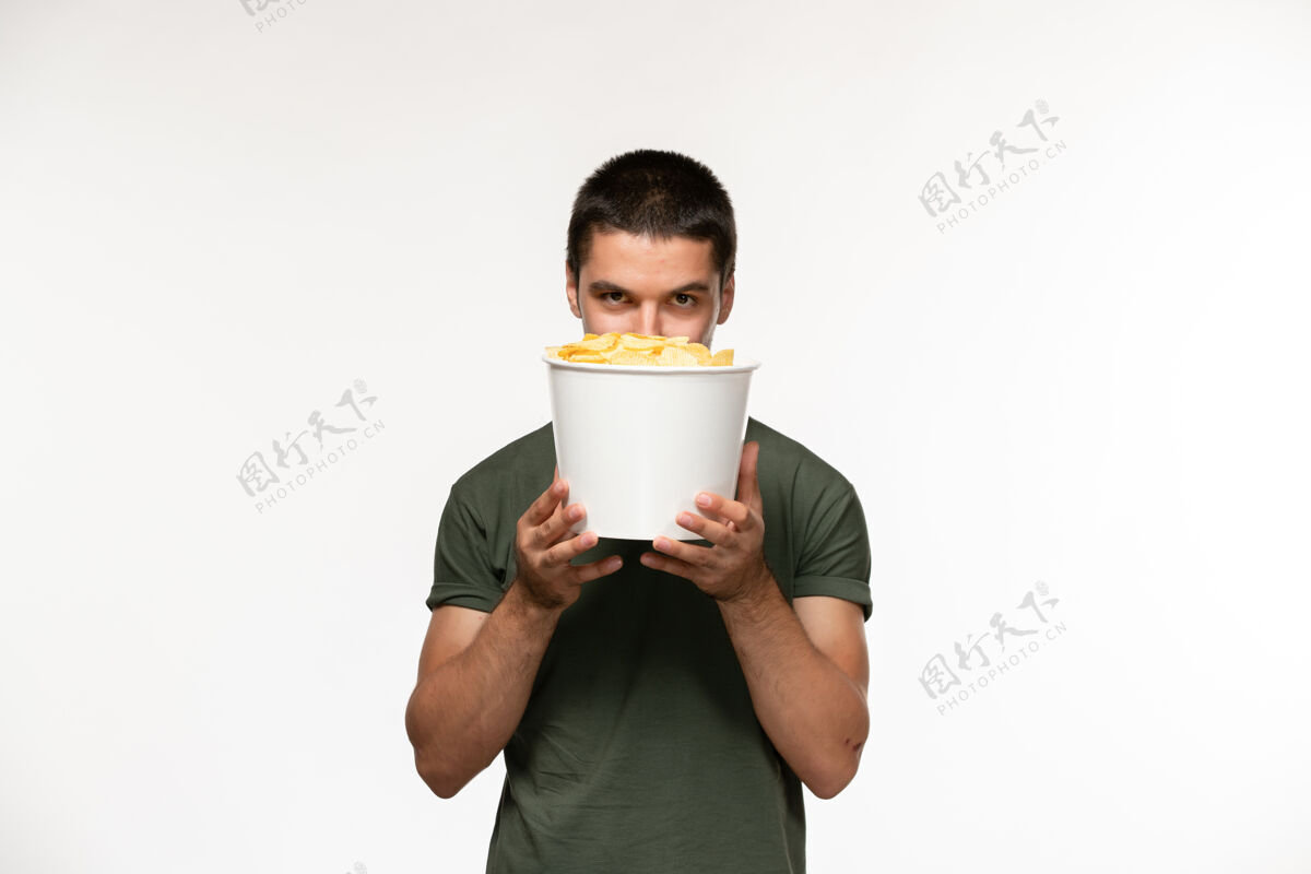 餐具正面图身着绿色t恤的年轻男性 白色墙上挂着土豆cips 孤独的人在电影院里电影冲压机浓缩咖啡