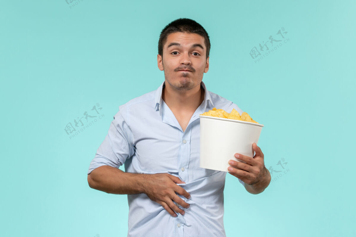 年轻人前视图年轻人拿着土豆cips在淡蓝色的墙上孤独的遥远的男性电影电影院电影电影肖像