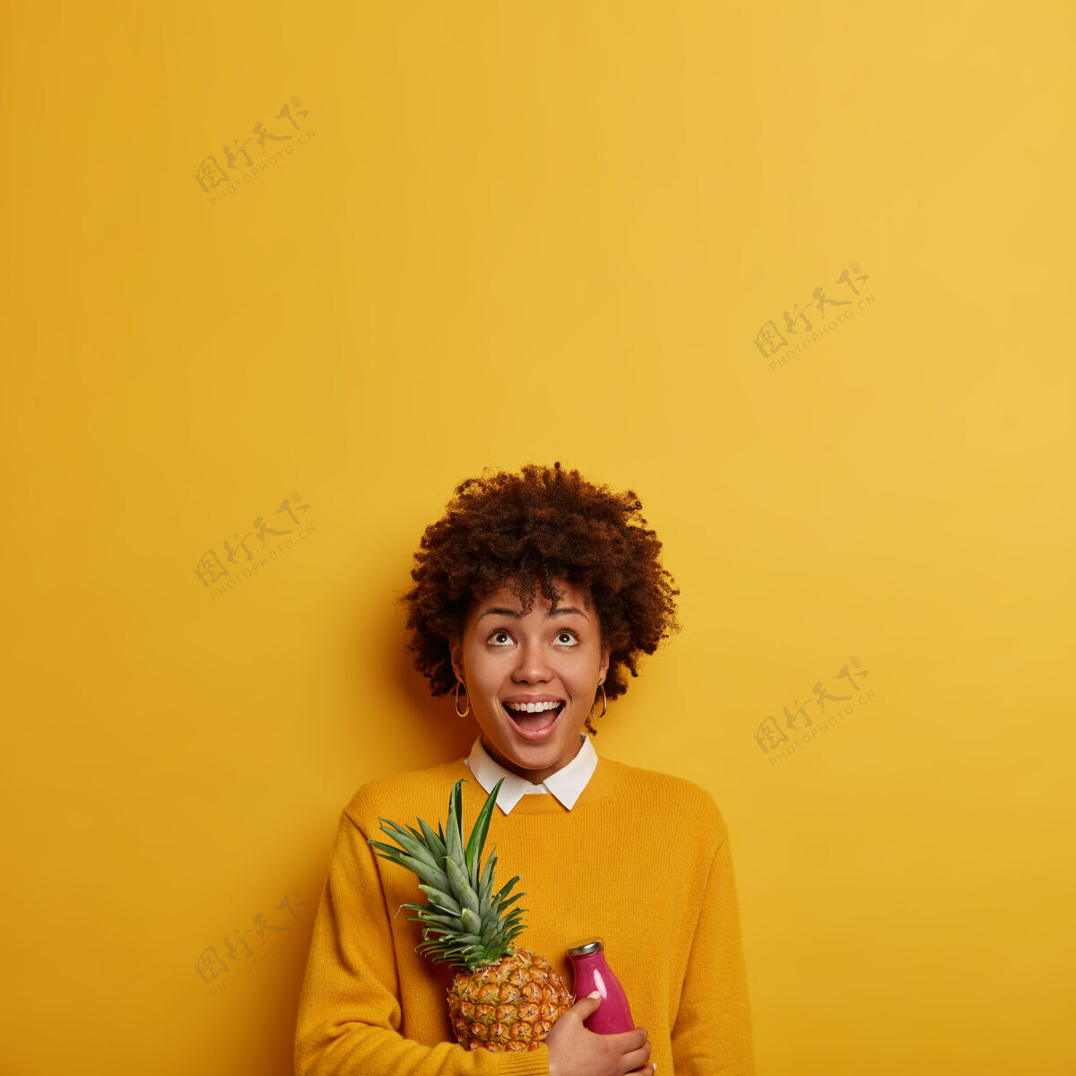 新鲜有趣的少数民族妇女的照片集中向上 持有新鲜的菠萝和冰沙 有健康的营养 穿着休闲服 隔离在明亮的黄色墙壁 为您的文字复制空间女人请高兴