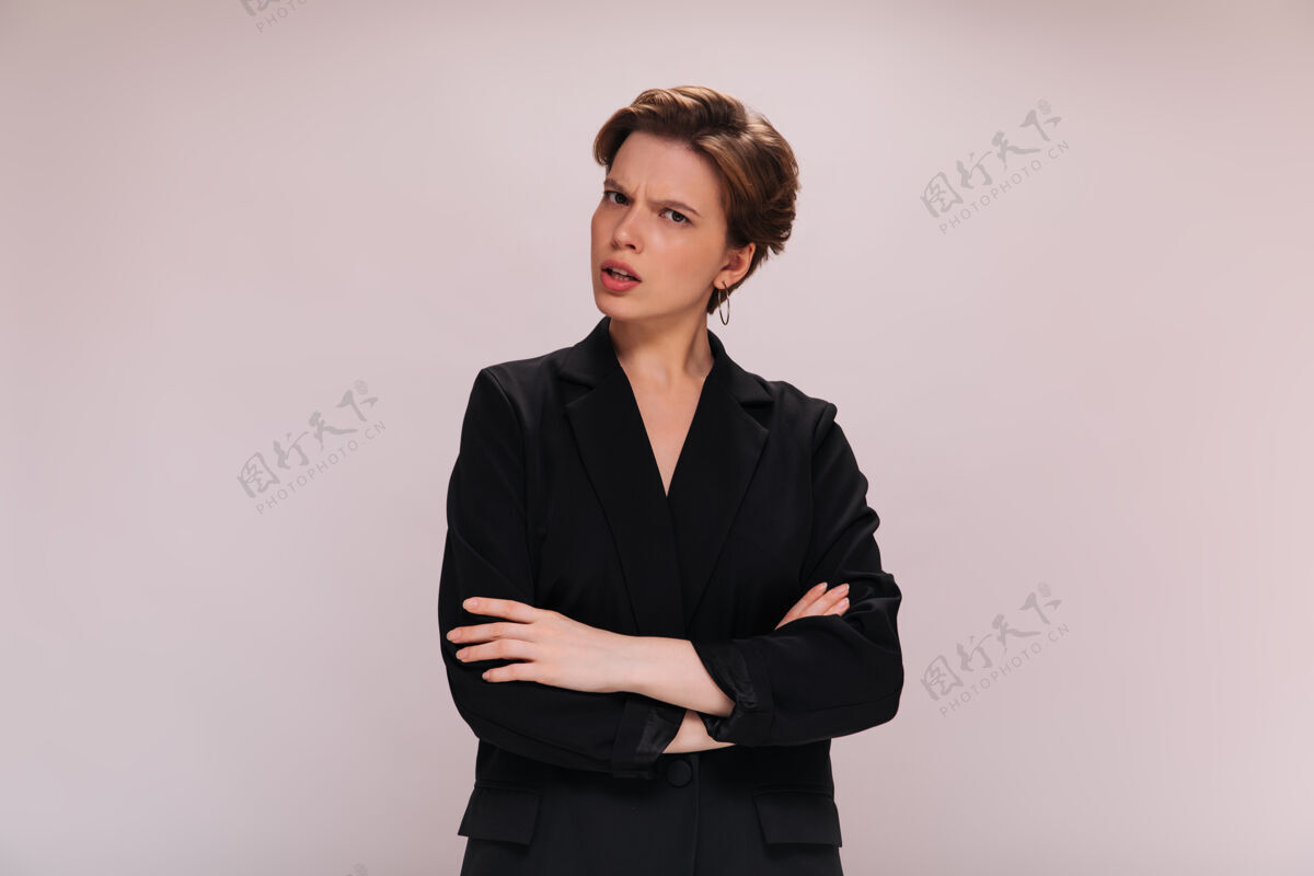时尚穿西装的短发女人误会地看着镜头穿黑夹克的女人在孤立的背景下心情不好地摆姿势正式优雅套装