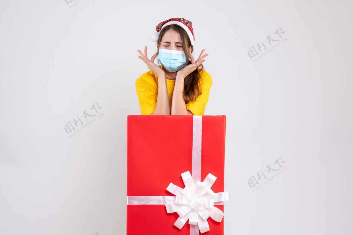 圣诞节前视图愤怒的女孩戴着圣诞帽闭上耳朵手指站在圣诞礼物后面手指人卡通