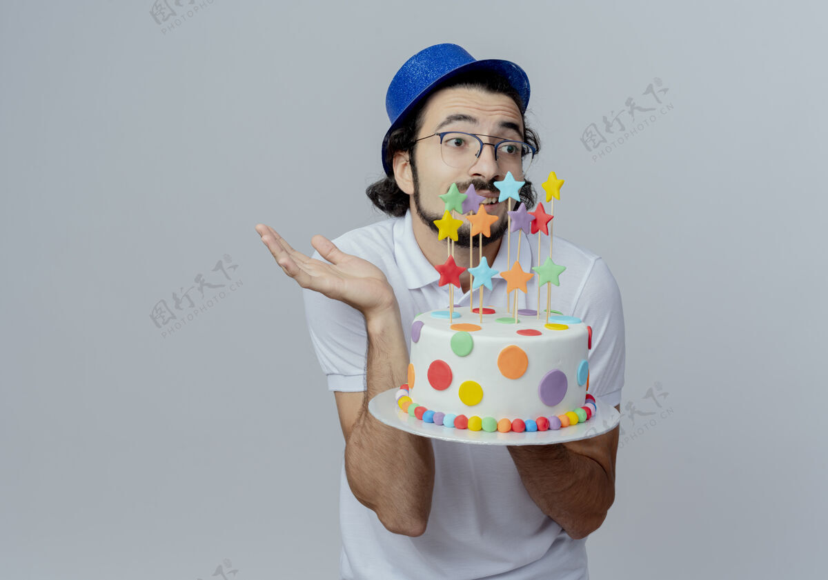 蛋糕看着身边迷茫的帅哥戴着眼镜和蓝帽子拿着蛋糕 摊开手隔离在白色的背景上摊开戴着帽子