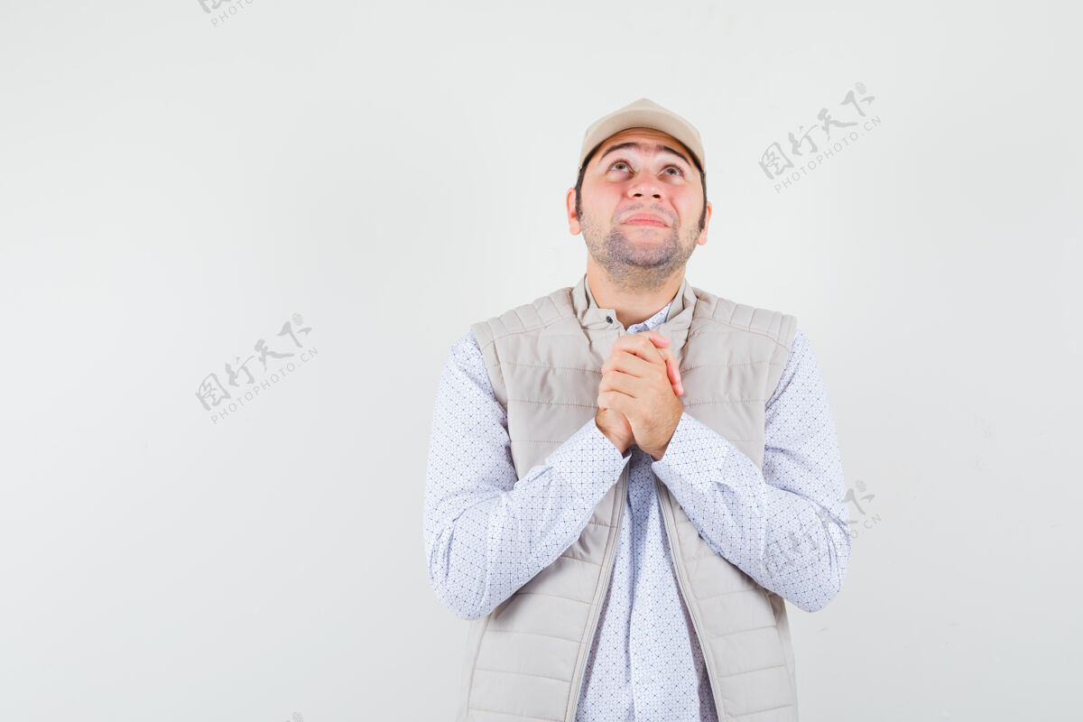 思想年轻人站在祈祷的姿势 向上看米色夹克和帽子 并期待着重点前视图胡须人花花公子