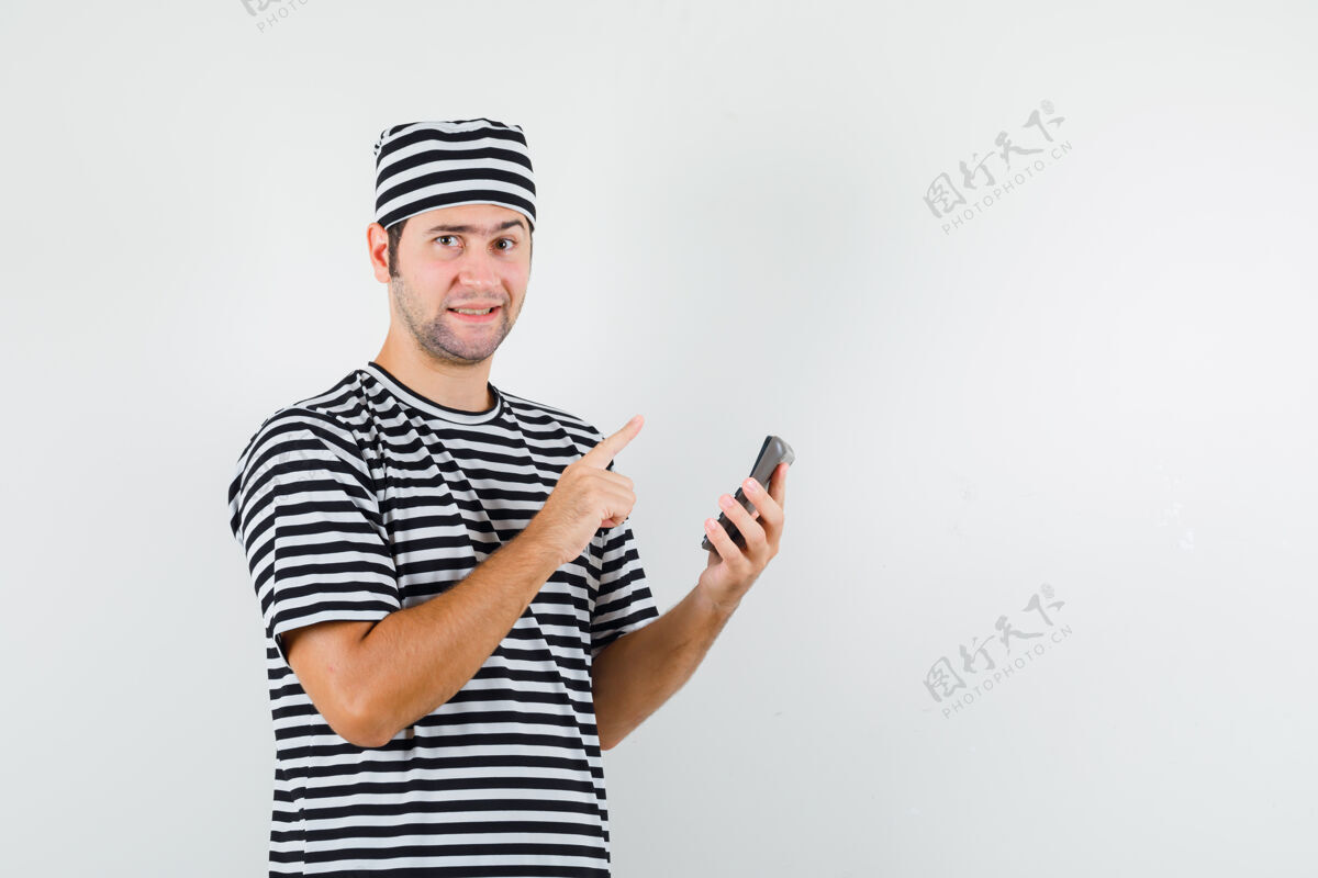 时尚年轻的男性指着上面 拿着一个穿着t恤 戴着帽子的计算器 看起来很理智正面视图男性休闲脸