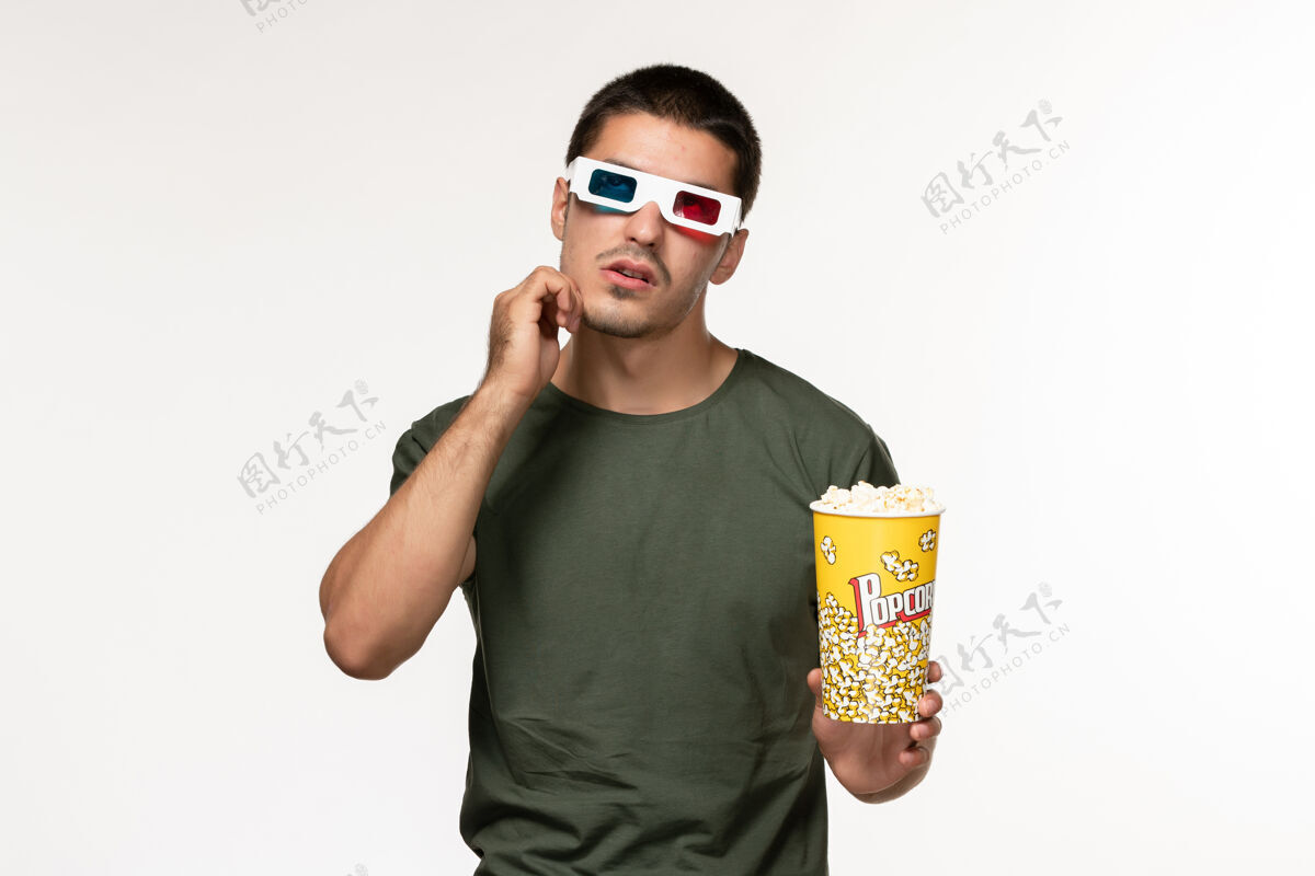 思考正面图身着绿色t恤的年轻男子戴着d型太阳镜拿着爆米花看电影思考白墙电影孤独电影院男性电影视图年轻男性电影