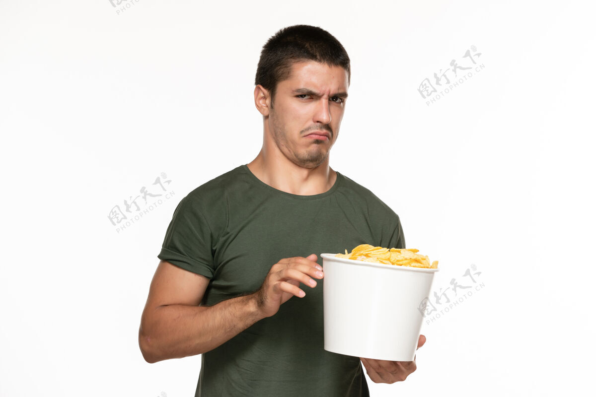 篮子正面图身穿绿色t恤的年轻男性拿着篮子和土豆 在白墙上吃着它们孤独地享受着电影享受电影土豆