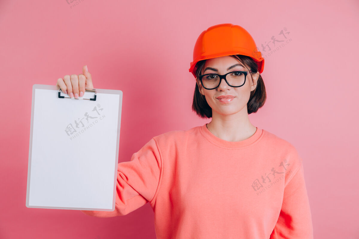 工程师面带微笑的女建筑工人手持白色的空白标志牌 背景是粉色的建筑头盔专业建筑复制