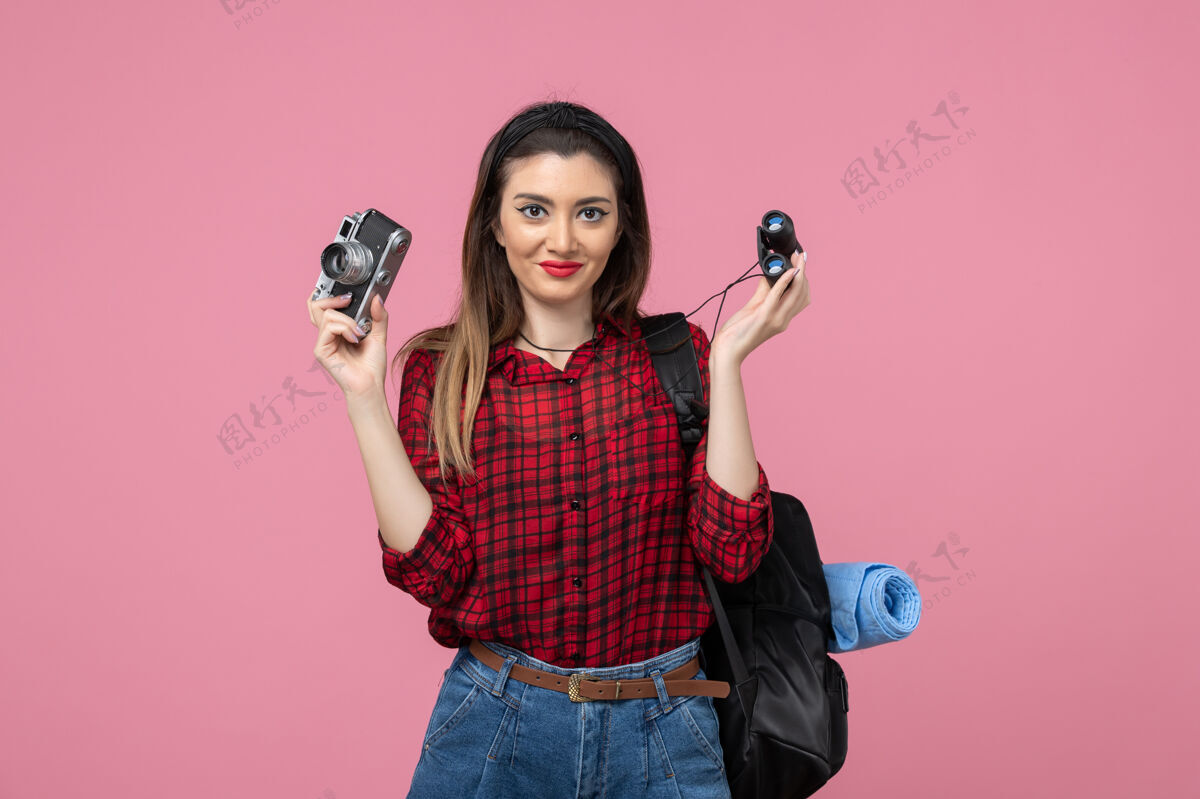 漂亮前视图年轻女性用双筒望远镜和相机在粉色背景上拍摄人色女人头发脸年轻女性