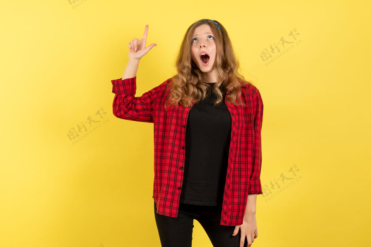 人正面图身着红色格子衬衫的年轻女性在黄色背景上摆姿势 看着天花板女孩的情绪模型颜色人类情感肖像姿势
