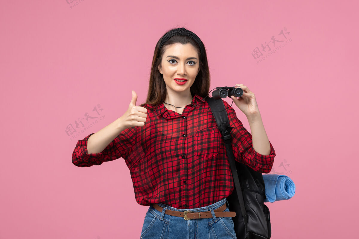 衬衫正面图穿红色衬衫的年轻女性用双筒望远镜在粉色背景上拍摄时尚色彩的女人黑发女士年轻女性