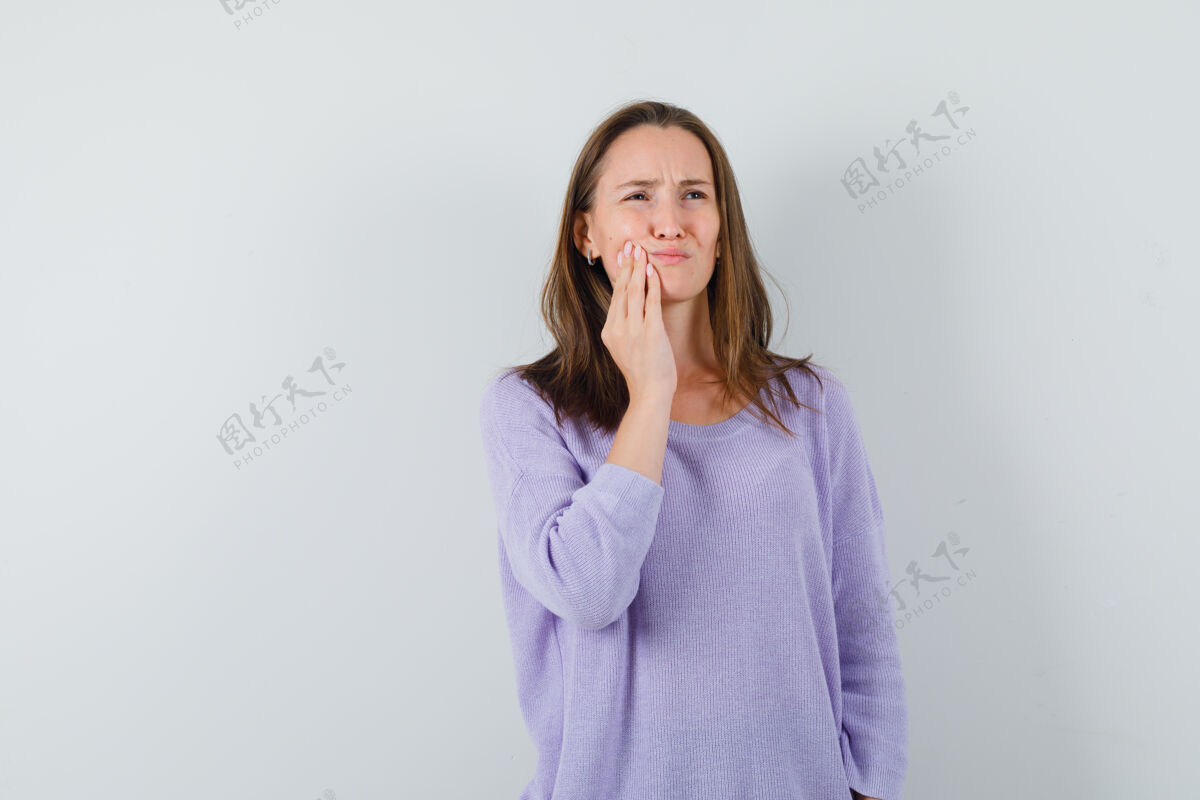 卷曲身穿淡紫色上衣的年轻女性患有牙痛 看起来很困扰正面图化妆漂亮性感