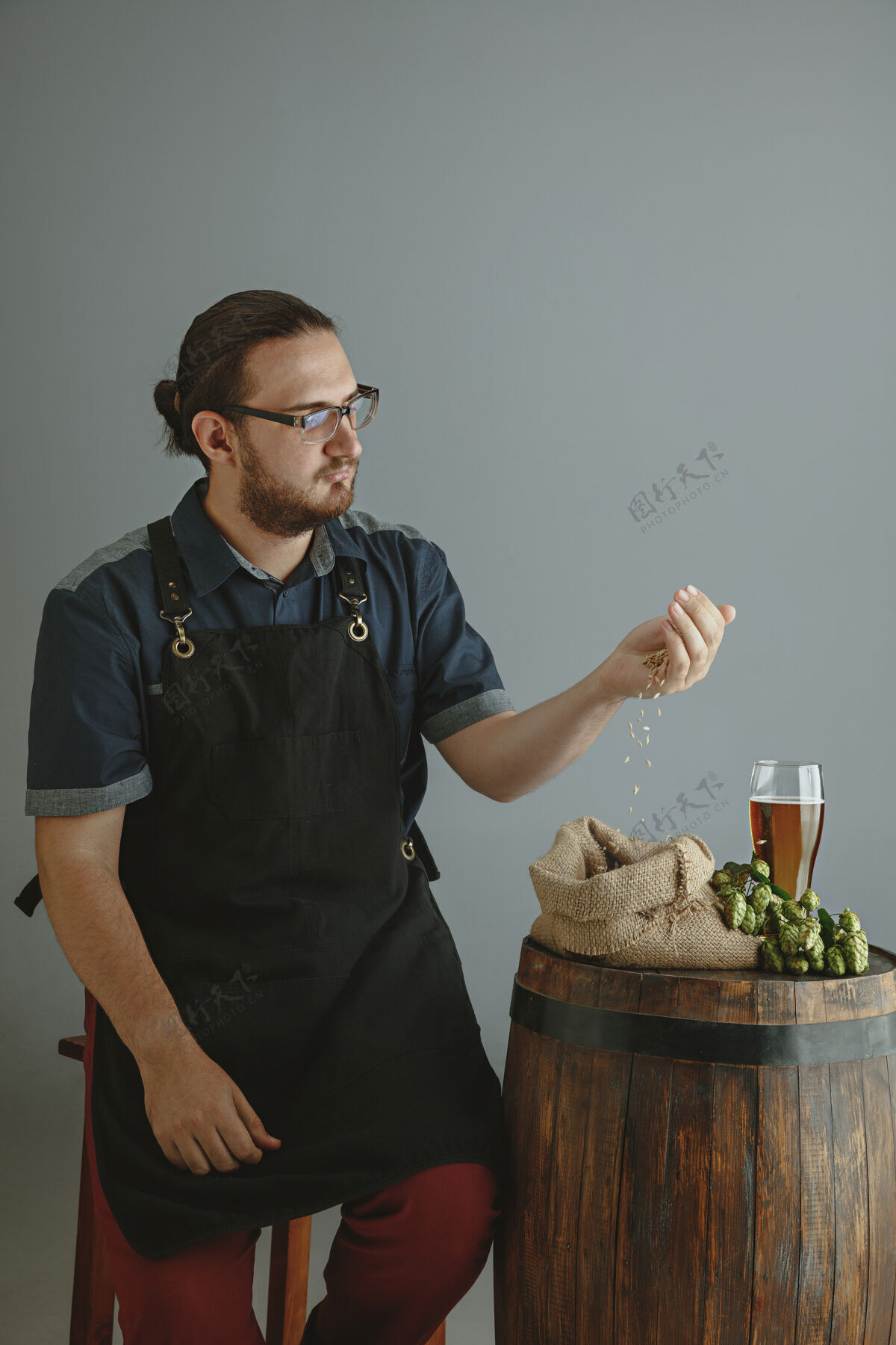 年轻人自信的年轻男性酿酒师 在灰色的木桶上用玻璃瓶自制啤酒人木材工厂