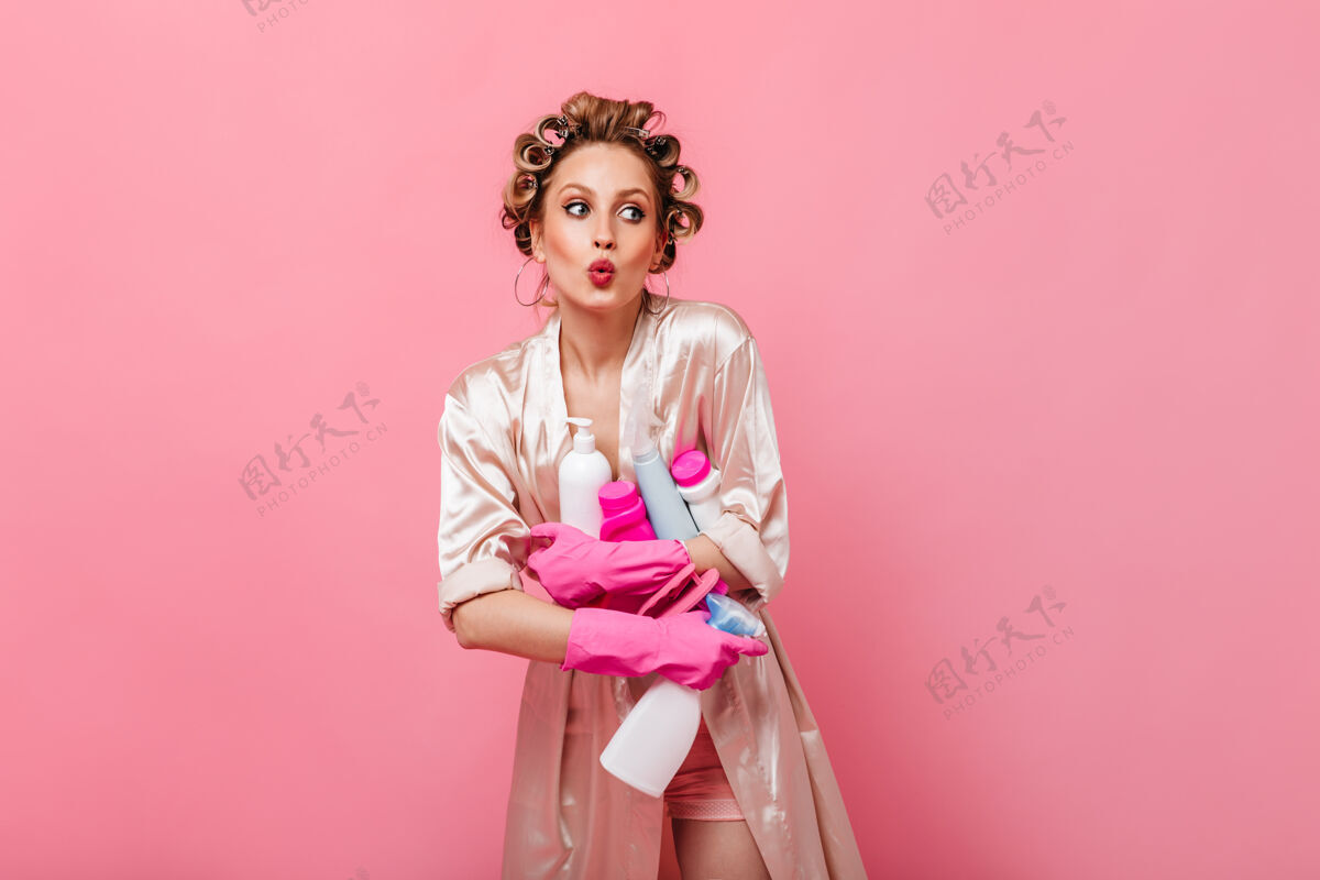 人穿着晨衣的女人吹口哨 把洗涤剂放在粉红色的墙上情感休息金发