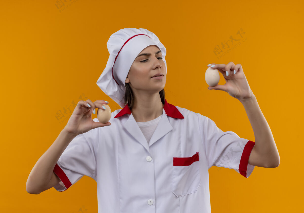 女孩穿着厨师制服的年轻自信的白人厨师女孩拿着并看着橙色的鸡蛋 留着复印空间厨师烹饪制服