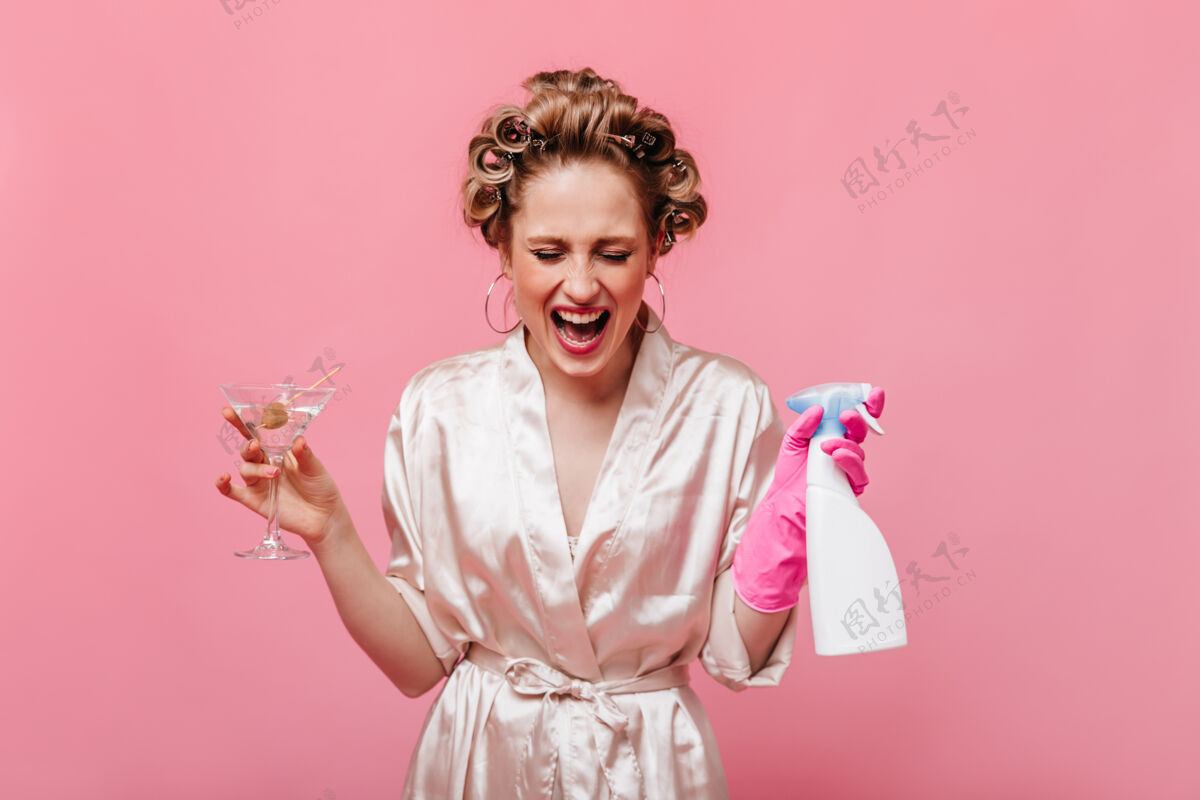 马提尼杯穿着粉红色长袍的金发女人拿着马提尼杯和洗涤剂摆姿势年轻美丽休息