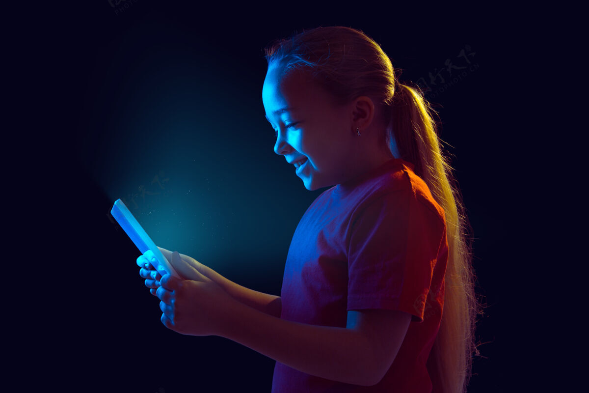 平板电脑微笑霓虹灯下隔离在黑暗墙上的白人女孩肖像使用平板电脑的美丽女性模特人类情感的概念 面部表情 销售 广告 现代科技 小玩意在线颜色工作