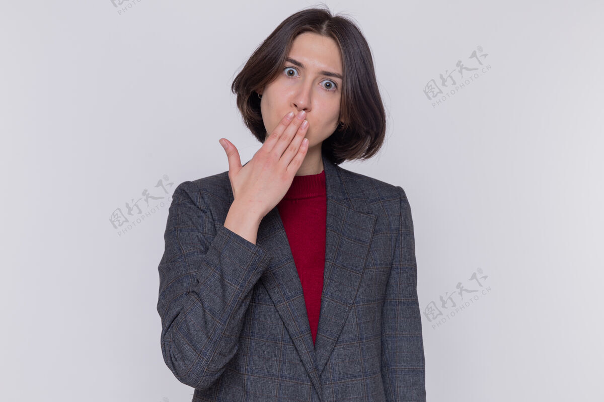 短裤一个穿着灰色夹克的短发年轻女人看着前面被震惊的捂着嘴站在白色的墙上嘴盖年轻