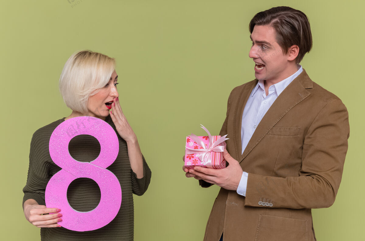 纸板年轻漂亮的情侣快乐的男人送礼物给他惊讶的女友站国际庆祝