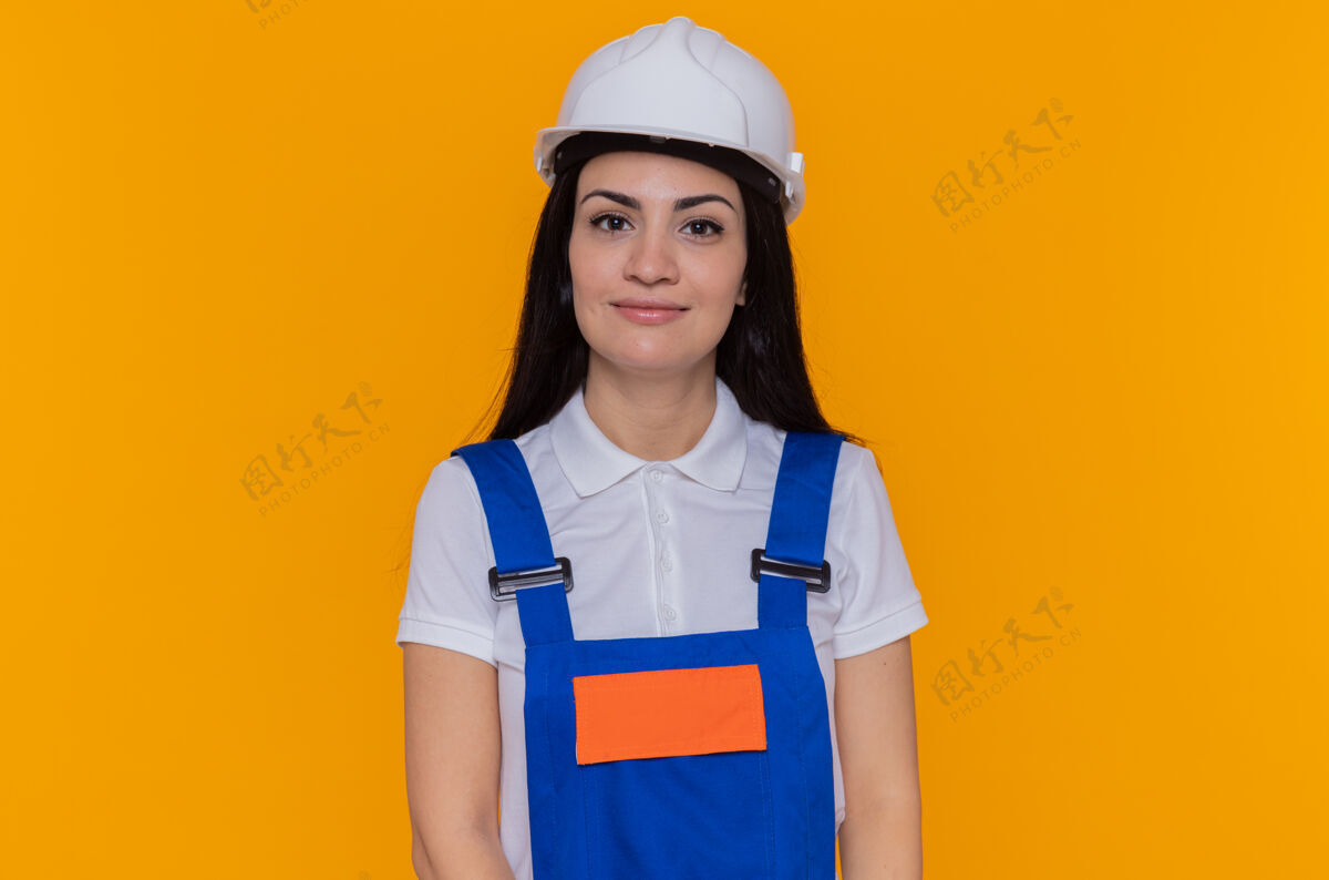 微笑身穿施工制服 头戴安全帽的年轻建筑工人站在橙色的墙上 面带微笑 自信地看着前方自信站立安全