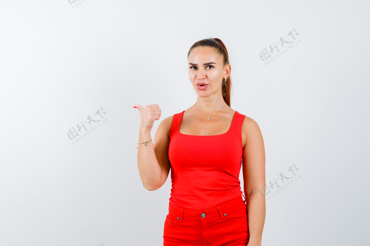 华丽年轻的女士大拇指在红色单品 红色裤子和看起来自信 前视图拇指前面积极