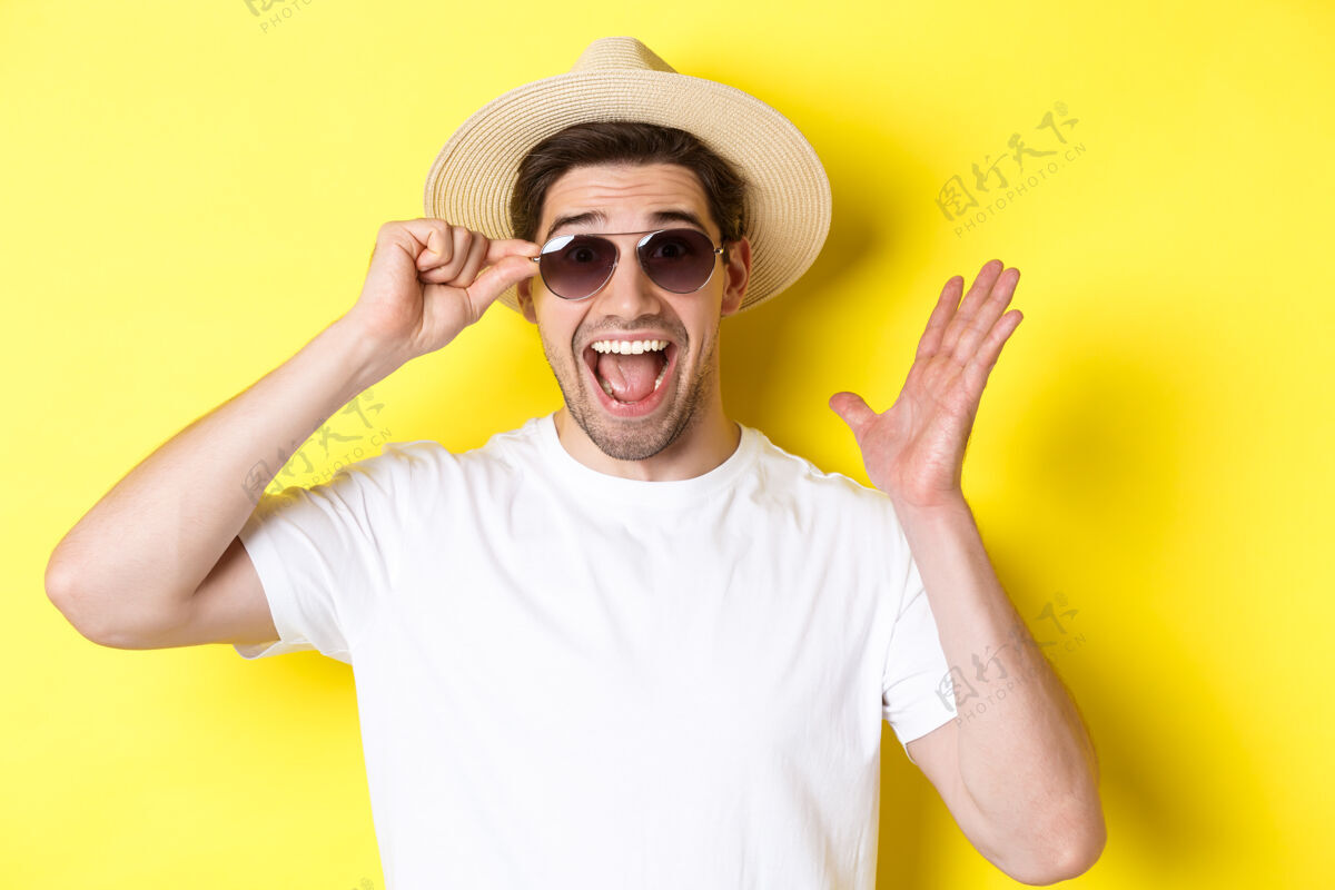 年轻人旅游和度假的概念特写镜头：惊喜的男人喊着快乐 享受着假期 戴着太阳镜 戴着夏天的帽子 黄色的背景男人男人黄色