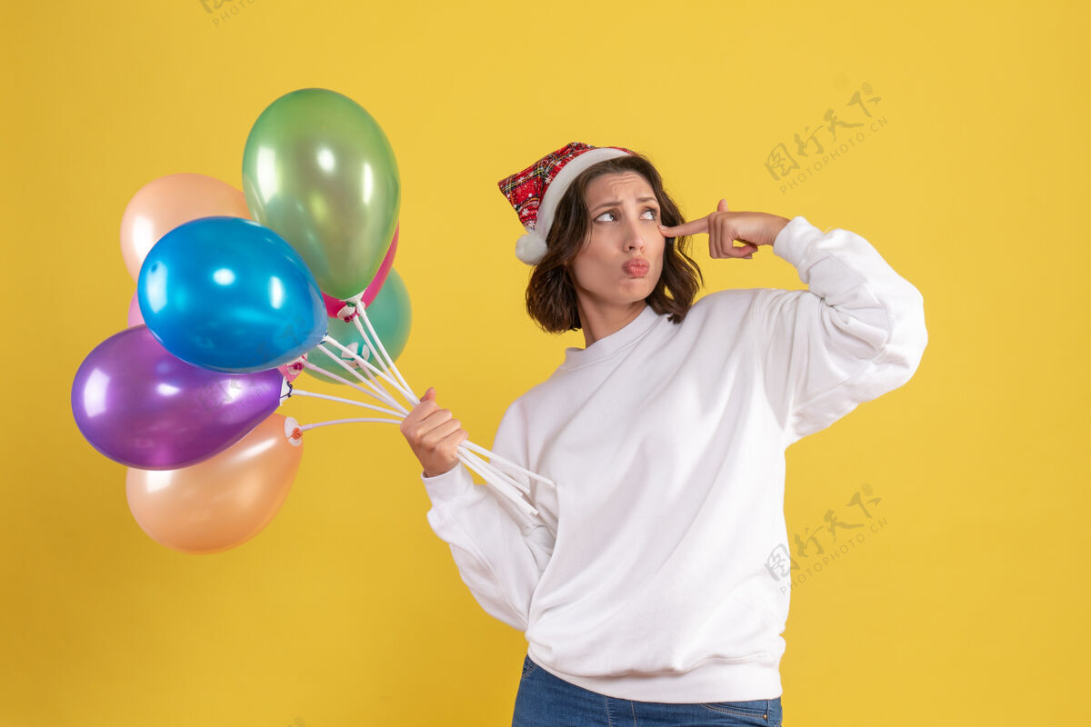 正面正面图年轻女子手持五颜六色的气球站在黄色的颜色年轻女人广播