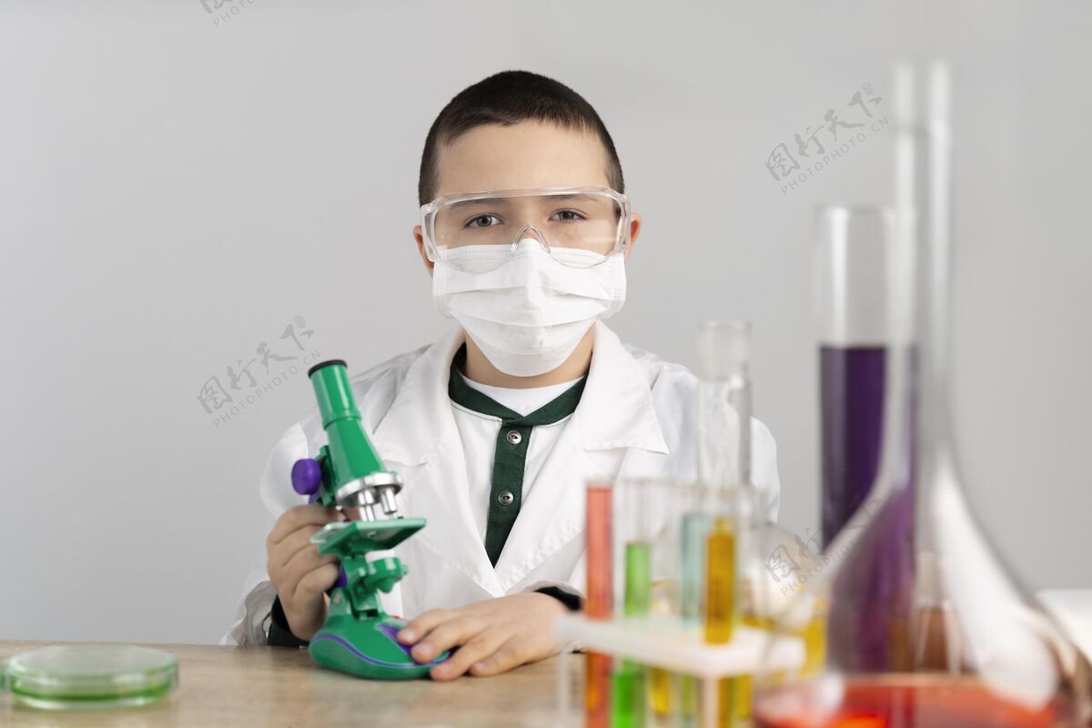 实验室外套实验室里拿显微镜的男孩科学科学防护眼镜