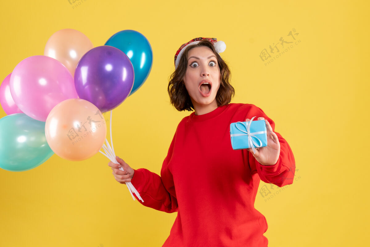 女人正面图年轻女子手持气球和小礼物在黄色圣诞假期新年情感色彩的女人派对礼物情感