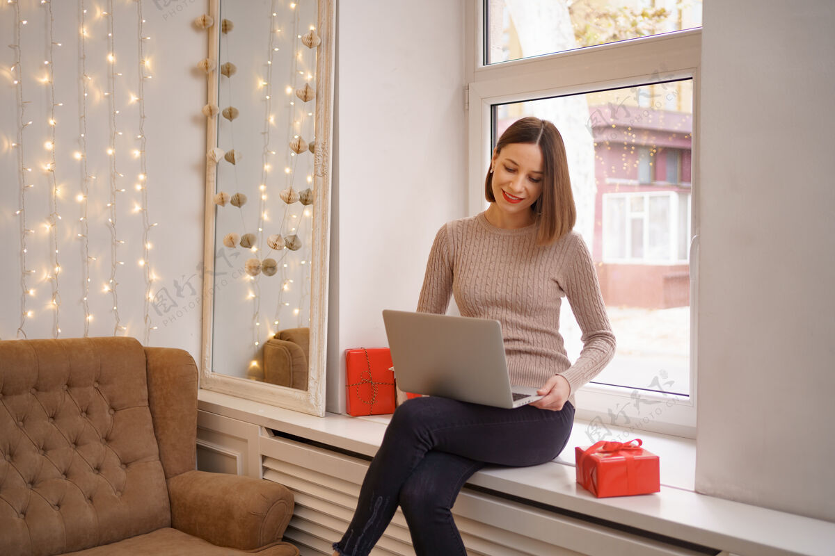 互联网带着礼品盒的笔记本电脑视频聊天中 微笑的年轻女子在向朋友致意网上购物圣诞节心情女性