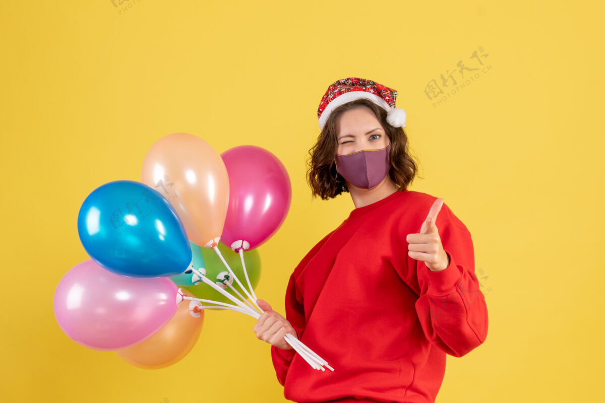 派对正面图：戴着黄色面具手持气球的年轻女子庆祝颜色外科面具