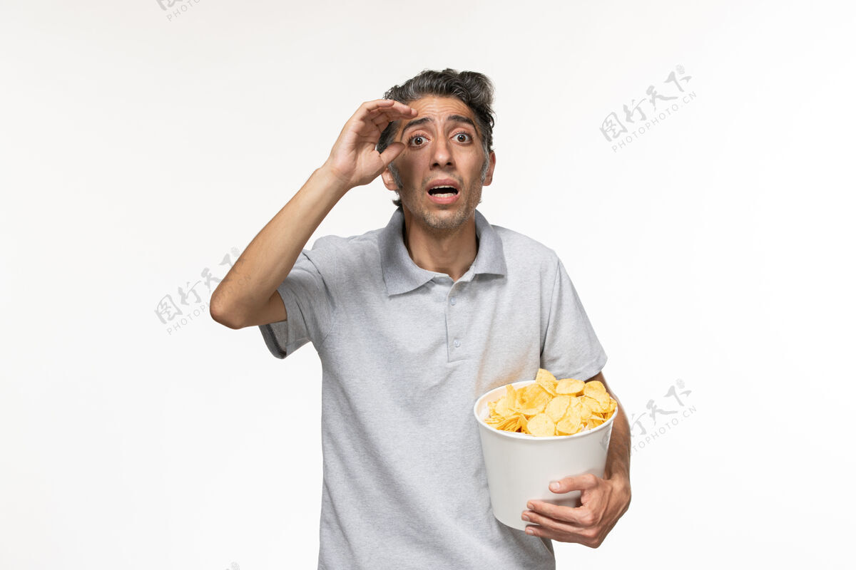 孤独正面图：白色表面上拿着薯片的年轻男性抱着食物遥远