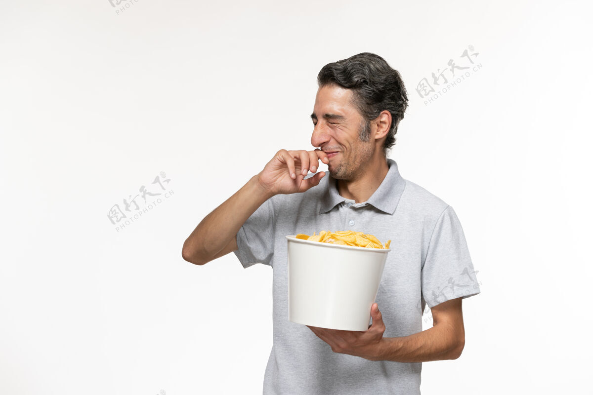 孤独正面图：年轻的男性正在吃薯片 在白色的表面上欢笑电影院杯子笑