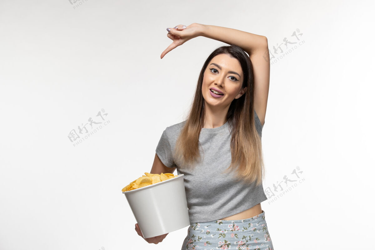 遥远正面图：年轻女性手持薯片在白色表面上看电影电影院看女