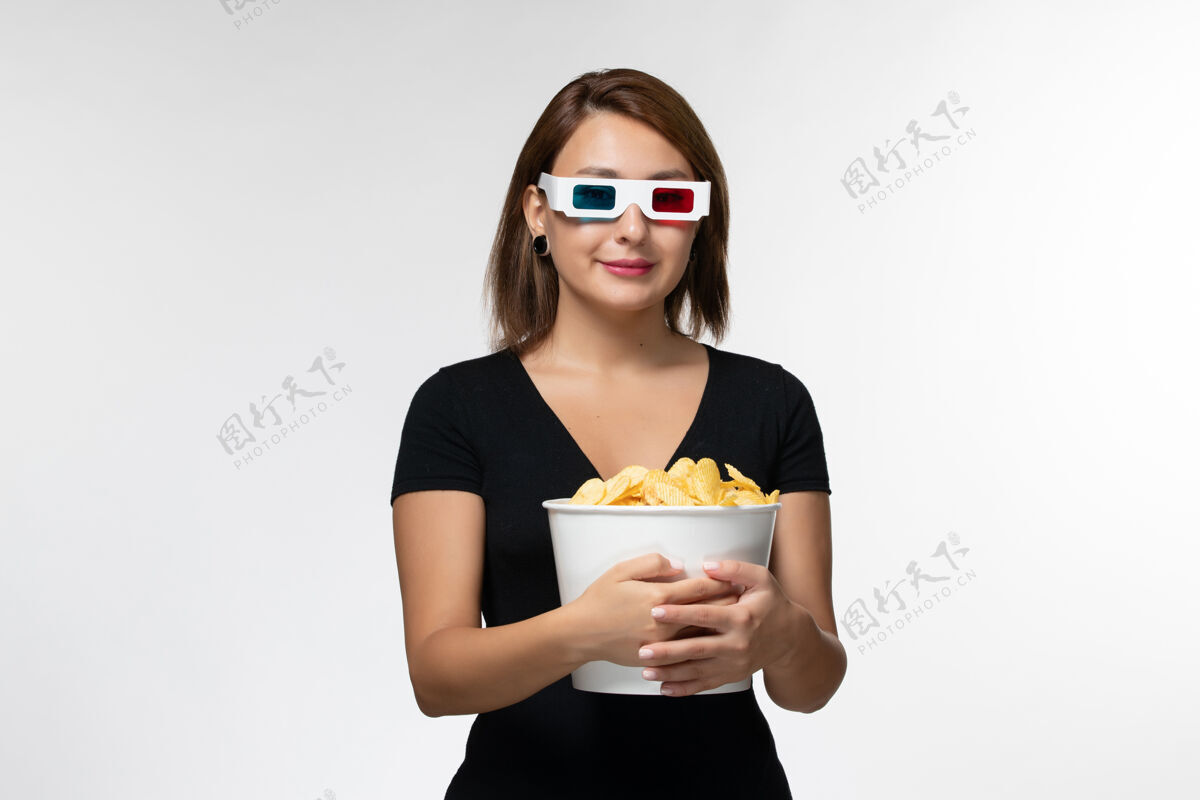 电影院正面图：戴着d型太阳镜拿着薯片的年轻女性 在白色的表面上微笑控股太阳镜孤独
