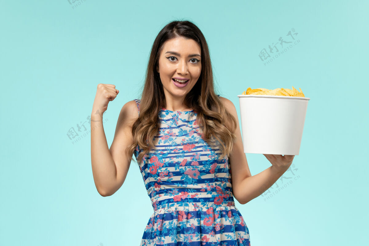 电影正面图年轻的女性拿着篮子和薯片 在蓝色的表面上欢欣鼓舞性感篮子土豆