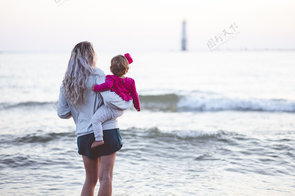大海特写镜头聚焦在一位母亲和她的孩子看海的背后年轻海景模糊