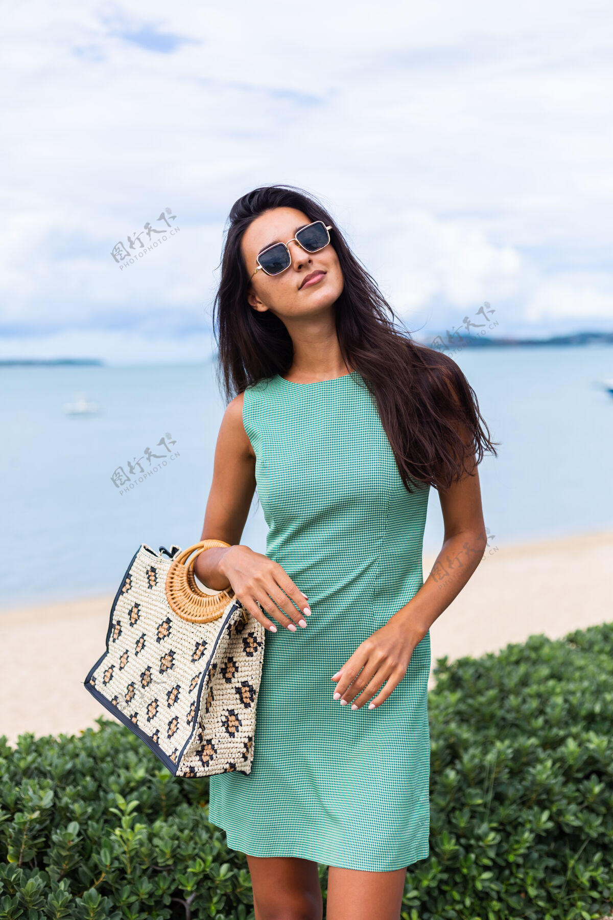 休闲漂亮时尚的快乐女人 穿着绿色夏装 带着包 度假时戴着太阳镜 背景是蓝色的大海夏天时尚度假