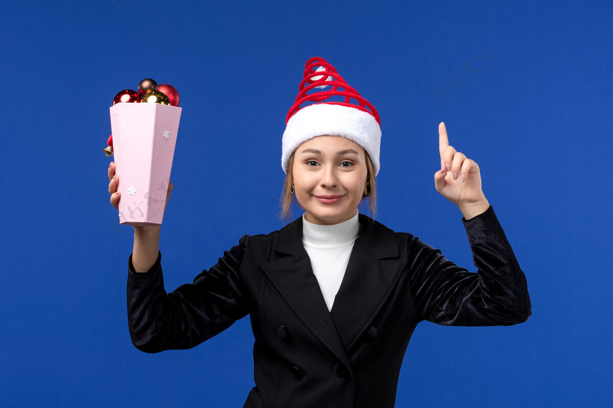 观点正面图：年轻的女性拿着树上的玩具在淡蓝色的墙上新年假期女性蓝色光圣诞节前面
