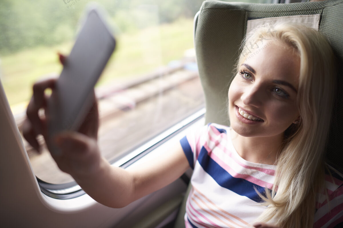 姿势在火车上自拍的金发女人休闲服相机乘客