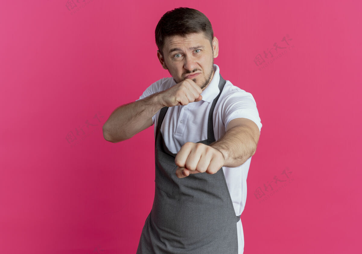 站围裙上的理发师站在粉红色的墙上 摆出一副握紧拳头的斗士模样围裙喜欢男人