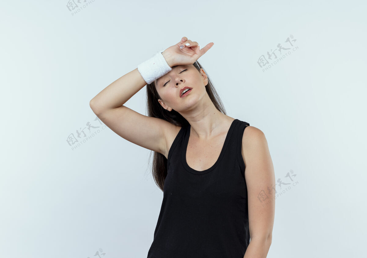疲倦戴着头巾的年轻健身女士站在白墙上 看起来很疲惫锻炼头带筋疲力尽