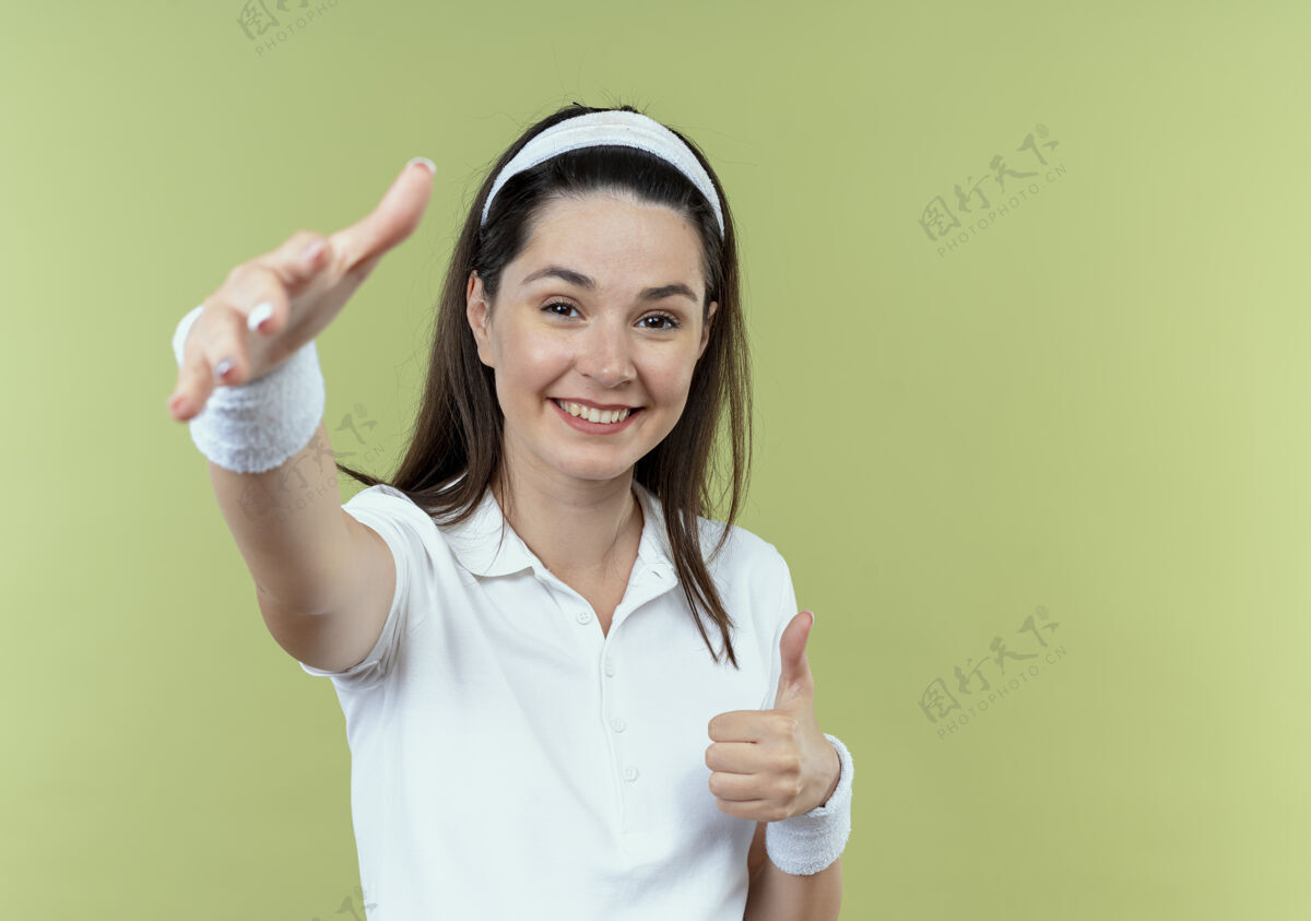 积极戴着头巾的年轻健身女士开心而积极地站在光墙上做欢迎手势手头带制造