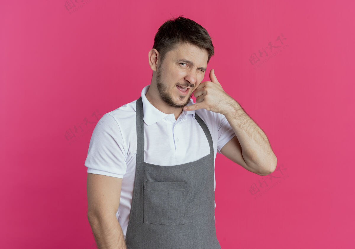 男人穿着围裙的理发师站在粉红色的墙上自信地做着叫我的手势自信手势制造