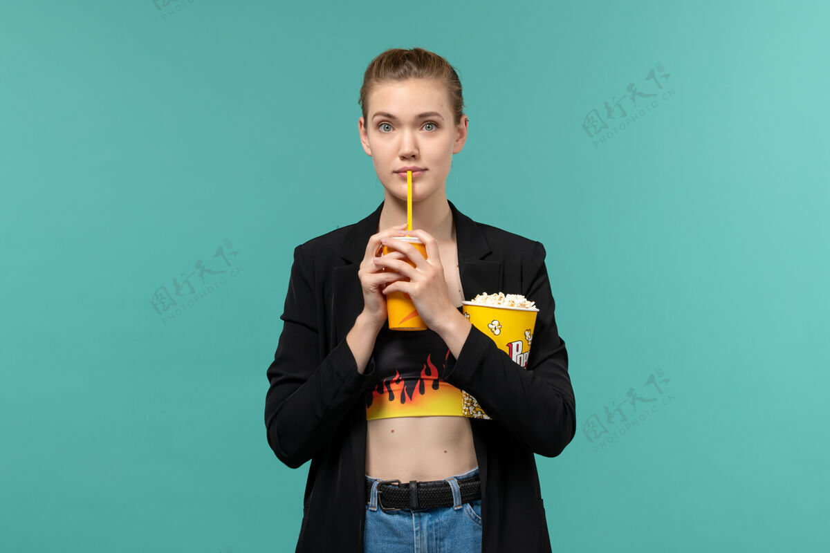 口哨正面图：年轻女子拿着爆米花喝酒 在蓝色的水面上看电影设备观看冰棍